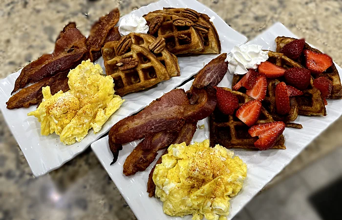 Waffles topped with pecans and strawberres, Scrambled Eggs, and a side of bacon